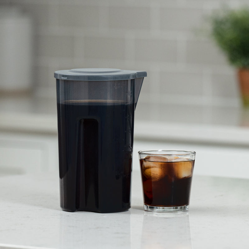 Pitcher of iced coffee next to a glass of iced coffee on a kitchen counter.